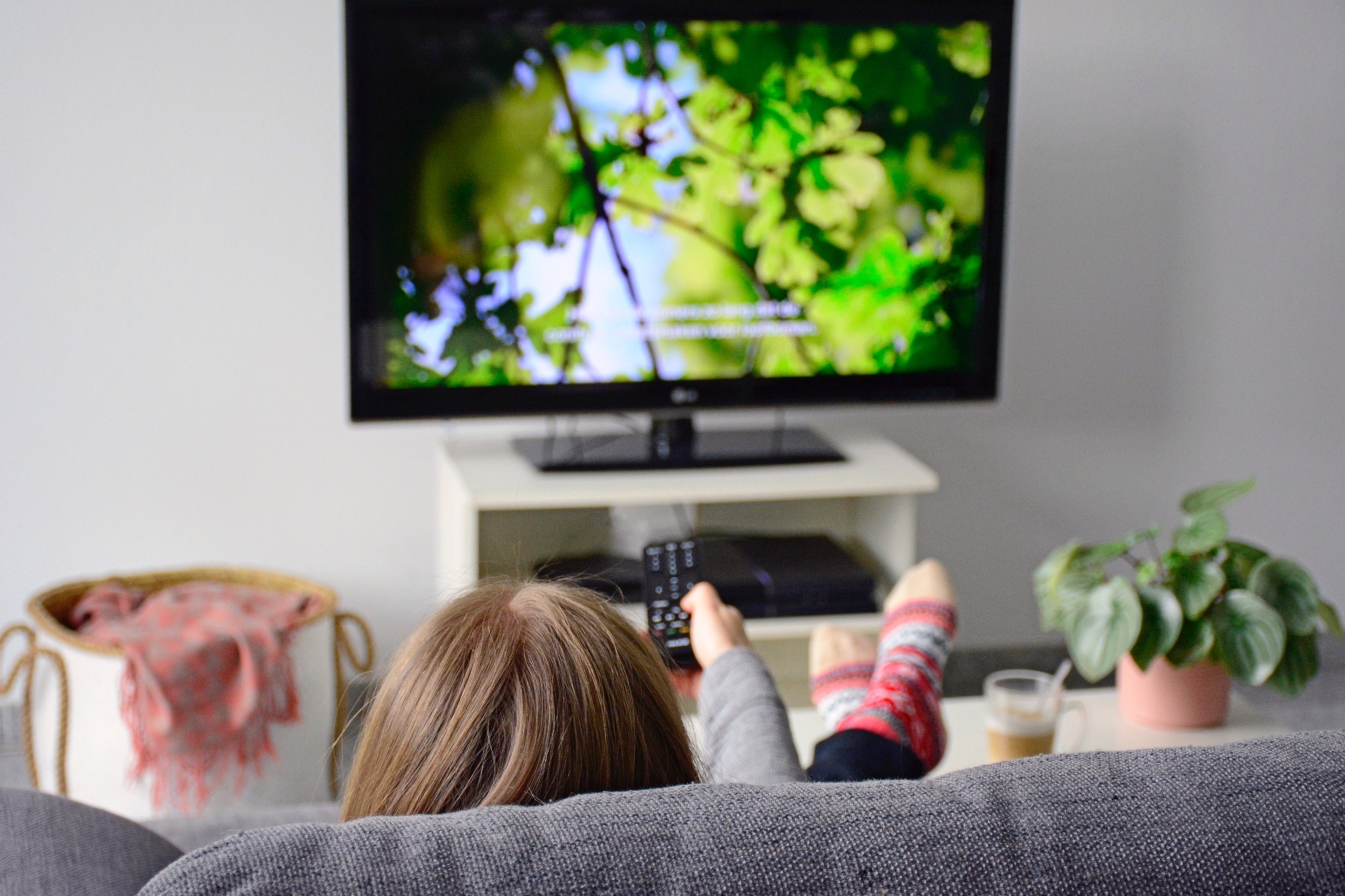 Eine junge Frau sieht von hinten fern mit Untertiteln, während sie auf dem Sofa im Wohnzimmer sitzt